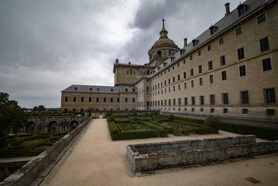 Dramatic view of El Escorial monastery and gardens under a cloudy sky. Located in Madrid, Spain.