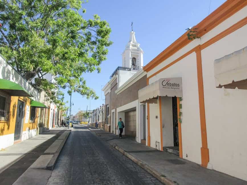 A scenic street view in Manzanillo, Colima featuring traditional architecture and a prominent bell tower.