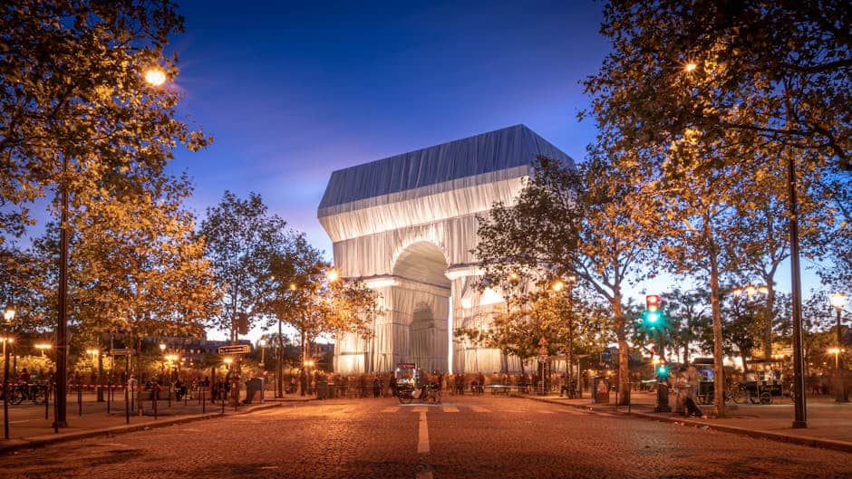 The iconic Arc de Triomphe wrapped in fabric, illuminated at night in Paris.