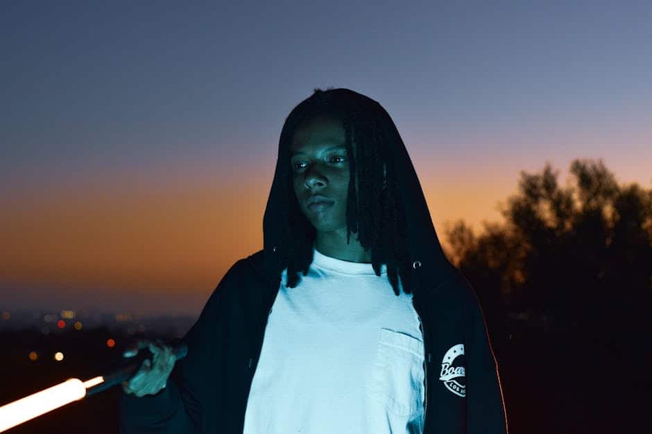 A young man with a hooded jacket stands outdoors at twilight in Los Angeles.