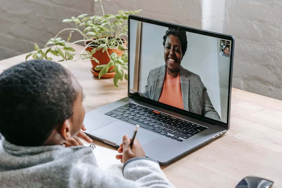 A child participates in online tutoring, focusing on a laptop screen with a smiling tutor.