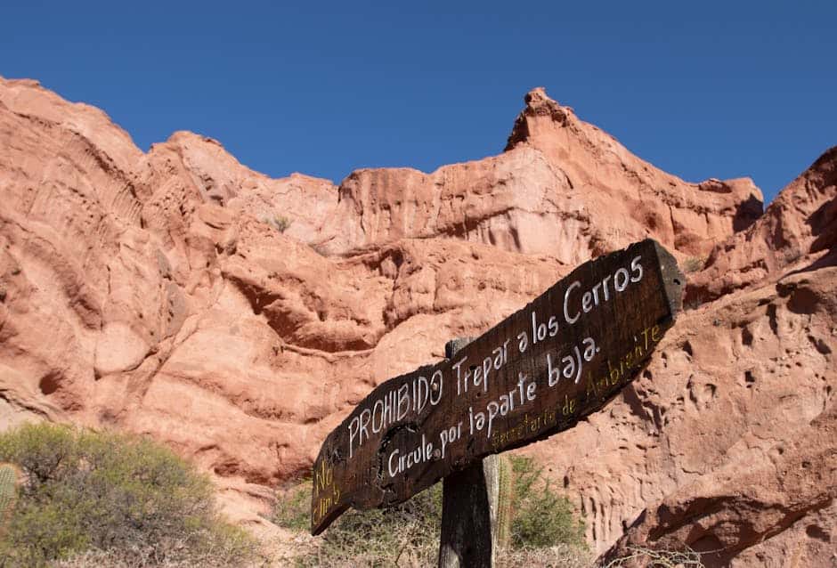 Wooden warning sign against climbing in rocky desert landscape with clear blue sky.