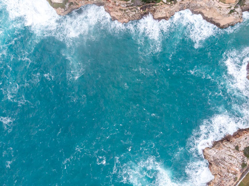 Drone shot capturing the vibrant blue waters and rocky coastline of Menorca, Spain.