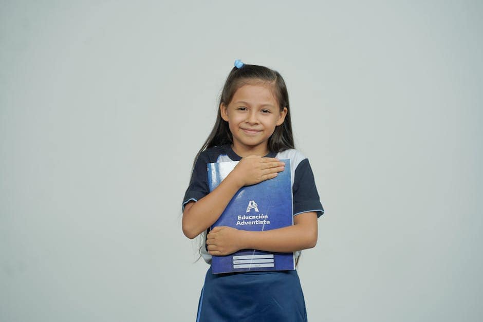 A young girl smiles while holding her school notebook, representing joy in education.